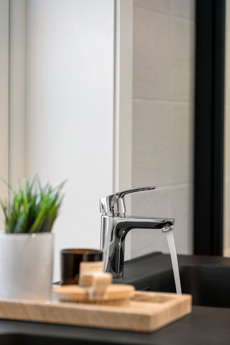 A sleek kitchen faucet with running water, potted plant, and soap on counter.