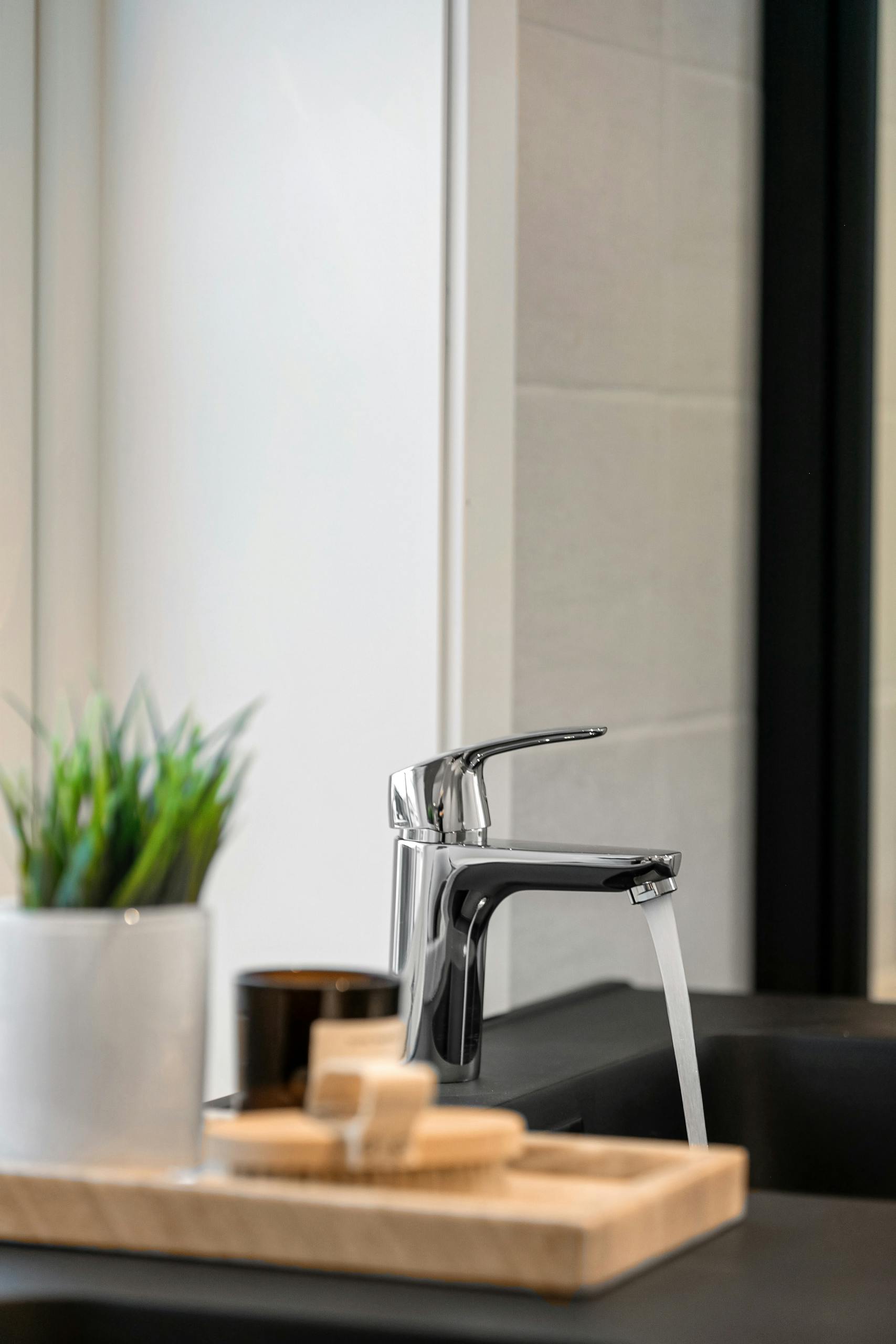 A sleek kitchen faucet with running water, potted plant, and soap on counter.