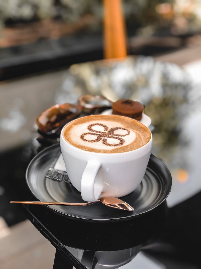 Close-up of a cappuccino with latte art on a black saucer with a teaspoon, shot outdoors.